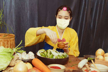 Beautiful Asian woman wearing a mask and a yellow hanbok loves to eat kimchi and cooks fresh, quality ingredients in a bowl.の写真素材