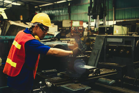 Male worker of engineering, lathing technician, wearing safety glasses, operating lathe, working overtime in an industrial factory  Selective focusの写真素材