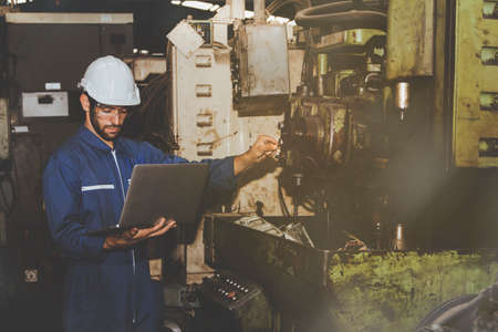 Engineer uses a laptop computer to check the date of service on old machines awaiting maintenance at the factory : Industrial engineer in a helmet inspects the maintenance process conceptの写真素材