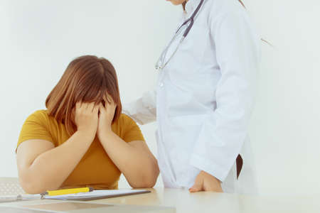 Medical care concept : Young Asian obese women are depressed and worried about their illness while the female doctor enters a positive shoulder and encourages them to treat the illness.の写真素材