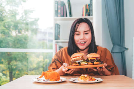 Asian woman enjoys fatty and cholesterol-rich fried chicken and hamburgers without worrying about her health.の写真素材