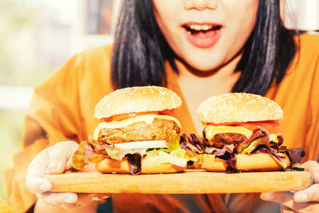 Concept of a large-scale woman : Hungry woman's mouth wants to eat two large marinated beef hamburgers. It's exciting and satisfying. Fast food on her favorite wooden tray.の写真素材