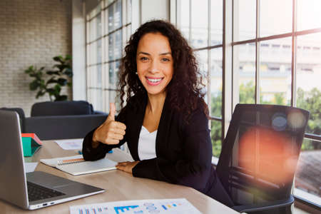 Start up portrait hipster businesswoman working with a bright smile and happy thumbs up while doing marketing and finance tasks in the office using a laptop computer.の写真素材
