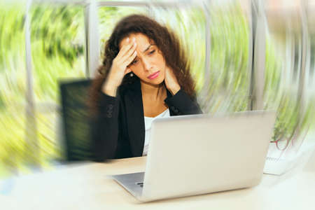 businesswoman experiences dizziness, headache, migraine lightheadedness and dizziness while sitting at her office desk : Chronic headaches that occur during work.の写真素材