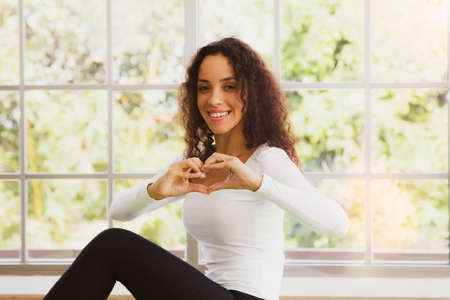 Portrait practicing yoga of a beautiful woman with wavy hair happy showing heart-shaped symbols with hands and friendly smiles sending love to everyone.の写真素材