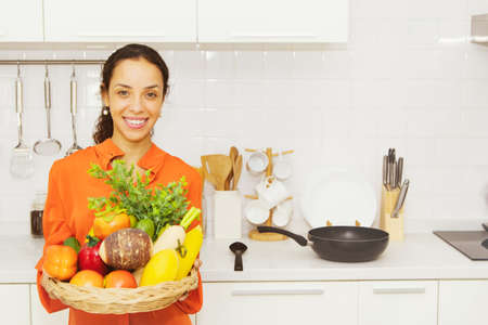 Happy hispanic smiling woman holding fruit tray in the kitchen : Portrait beautiful spanish femele who is a housewife dressed in colorful clothes, relaxed mood, smiling at the camera is charming.の写真素材