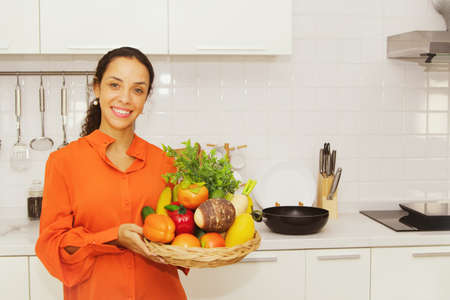 Happy hispanic smiling woman holding fruit tray in the kitchen : Portrait of a beautiful woman who is a housewife dressed in colorful clothes, relaxed mood, smiling at the camera is charming.の写真素材
