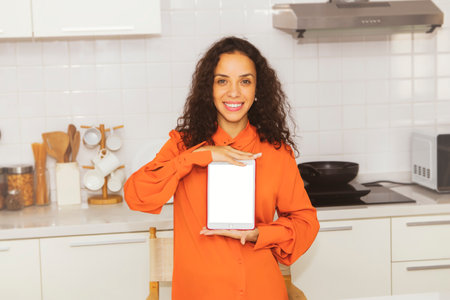 Happy curly-haired portrait Latin American woman holding a laptop on a white background in an old rose shirt smiling happily in the kitchen.の写真素材