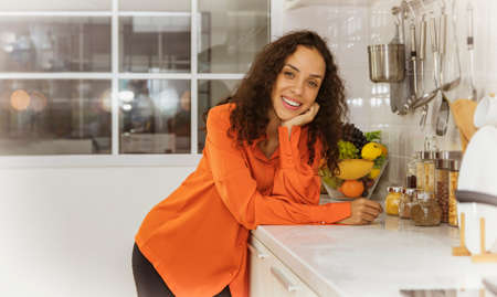 Portrait beautiful Latin American housewife with happy good mood, think positive, look at the camera, stand near the gas stove to cook in the kitchen at home.の写真素材