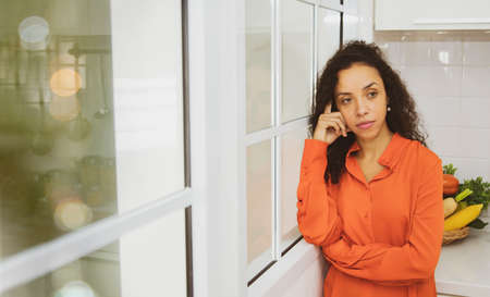 Thoughtful mature womanconcept : Portrait latino housewife stands in the kitchen contemplating something deep in her kitchen, thinking about making an upcoming family dinner.の写真素材
