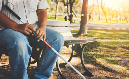 Elderly blind man with a blind cane sits alone on a park bench : Lind man who wants peace and lives in solitude concept.の写真素材