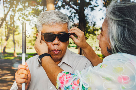 Senior couple caring for blind lovers concept : Wife is beside the blind old man to help by wearing dark glasses to block the light and ultraviolet rays from lovingly destroying her husband's eyes.の写真素材