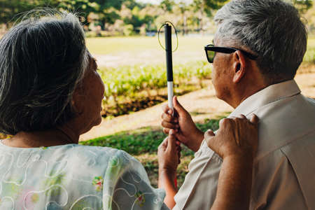 Senior couple caring for blind lovers concept : Back view senior wife touched her husband's shoulder with her hand to encourage, caring, and lovingly care for him while he rested in the garden.の写真素材