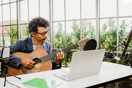 Male classical guitar teacher sits in class recording lessons and lessons on a laptop to prepare students online for courses during the pandemic : Concept  education online teaching.の写真素材