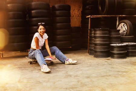 Young Asian woman in a good mood sits on a skateboard while working in a relaxed atmosphere.の写真素材