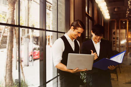 The handsome business partners, two white businessmen working in Asia and foreigners working positively, and working together to create a business plan during a coffee shop consultation.の写真素材