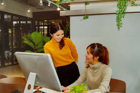 Two Asian business women gathered, looking friendly, working together in an office friendly manner.の写真素材