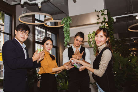 Group of colleagues, office workers and businessmen stand up to playfully clean their hands and fingers together using liquid alcoholの写真素材