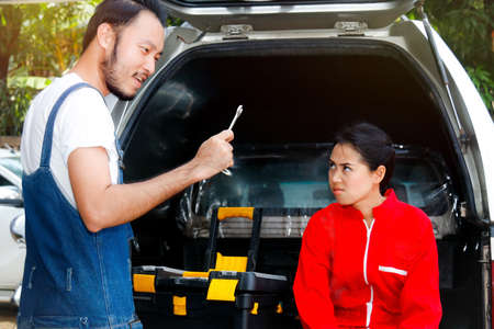 Couples, car mechanics, technicians, men and women are quarreling : Man and woman mechanic couple quarrel while working to find the missing wrench as the man finds it and mocks.の写真素材