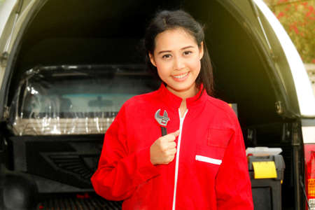 Portrait professional Asian female mechanic in a red uniform holds a wrench to check the engine of a diesel pick-up truck to be ready for use : Mechanic engineer woman working in a car repair station.の写真素材