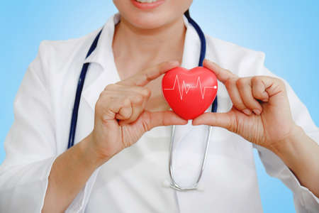 Female doctor with a stethoscope holding a heart, a white pulse in her arms. The concept of care for...