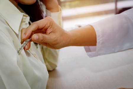 Female doctor's hand examines the body using a mercury thermometer to measure the temperature of a cold patient who is admitted to the hospital.の写真素材
