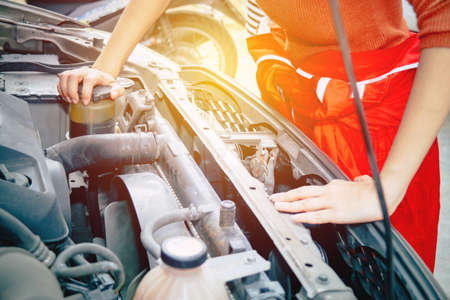 Professional Asian female mechanic in a red uniform checks the oil level of the diesel pickup truck to make sure it is ready for use : Mechanic engineer woman working in a car repair station.の写真素材