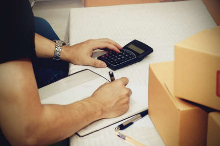 Men are sitting using the money calculator, to log a notebook for fees and mail delivery expenses.の写真素材