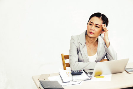 Portrait of middle-aged business woman using thoughts sitting on the desk with anxiety.の写真素材