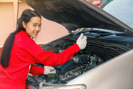 Portrait asian female mechanic in a red uniform checks the oil level of a diesel pickup with...