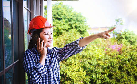 Female architects work outside the building, use phone, communicate and gesture pointing fingers to the foreground.の写真素材