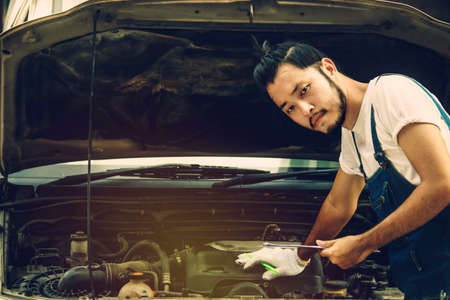 Concept of car maintenance in service stations : The male mechanic writes down the checklist for revision and verifies the scheduled use conditions and maintenance history.の写真素材