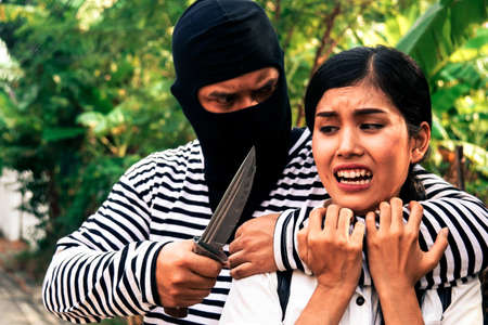 Crime concept : Robbers use force and knives to attack a young woman to harass the woman walking alone, and the woman terrifies and screams against fear.の写真素材