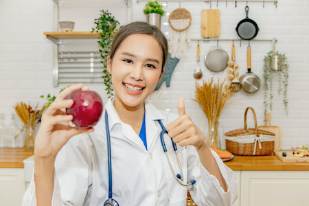 Vibrant and healthy beautiful asian woman nutritionist doctor thumbs up showing red apple, miracle fruit with vitamin C, excellent nutrition, good for health, nutrition advice in tの写真素材