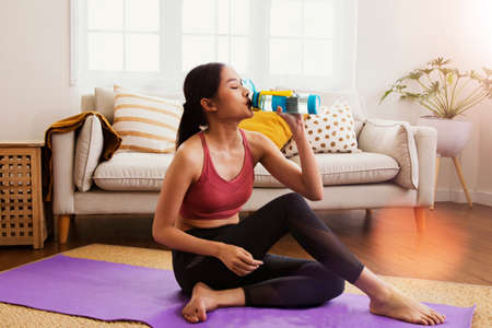 Health care beautiful asian female model sits and exercises yoga loses weight sits to drink clean water mixed with mineral salts to relieve thirst to refresh after losing energy anの写真素材