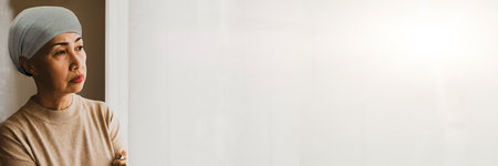 Elderly asian woman wearing headscarf to cover her baldness from cancer with chemo chemotherapy : Portrait senior woman with brain tumor stood looking out of the window anxiously tの写真素材