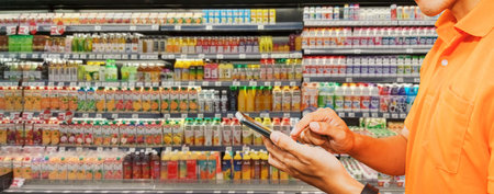 Behind the scenes work of a food delivery man with smartphone taking orders from customers who order food in the supermarket by shopping for juice quality products in the online suの写真素材