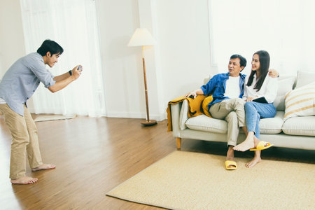 Happy family : Brother takes pictures of father and sister enjoying the relationship of Asian families in the living room together for a fun photoshoot : Family day conceptの写真素材