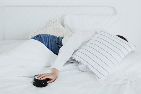late night woman : Lazy girl spent the night in bed put on jeans without changing her clothes covered her face with pillows slept and woke up late using her hands to turn off the aの写真素材
