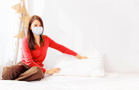 Asian women wearing masks to prevent allergies from dust and dust mites, put pillows, blankets and bedspreads on the mattress of the bedroom at home to keep it clean : Daily housewの写真素材