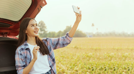 Happy asian female tourist takes a selfie in a car as she drives on an agricultural drive to tour the fertile corn fields following the COVID-19 outbreak : Conservation tourism conの写真素材