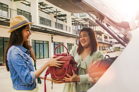 Girl friends help each other to pack luggage in the car with their friendship : Two young women dressed casually on vacation, drove off on a weekend trip, packed their suitcases toの写真素材