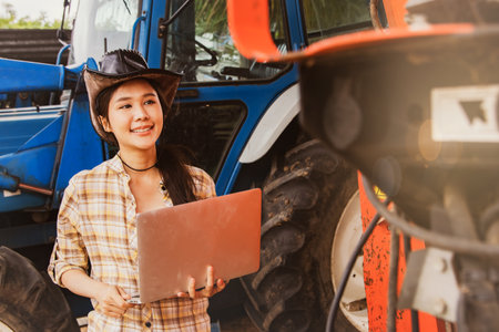 Asian woman farmer smile, agribusiness and livestock operator holding laptops to inspect machines and tractors for agricultural use, inspect maintenance services and use on agriculの写真素材