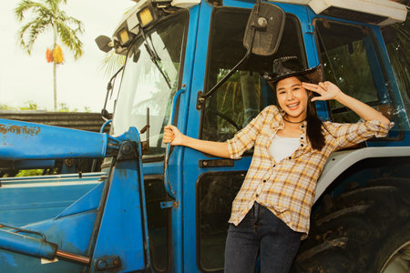Asian young woman farmer enjoys her work in the field, standing on a tractor to drive to harvest the harvest in the morning plantation : Portrait woman with a career in agricultureの写真素材