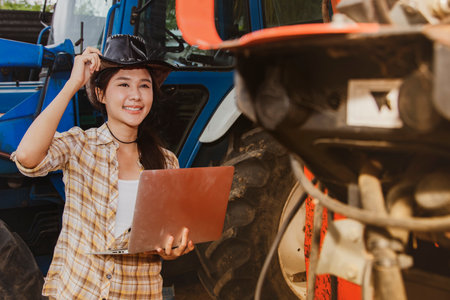 Asian woman farmer, agribusiness and livestock operator holding laptops to inspect machines and tractors for agricultural use, inspect maintenance services and use on agriculturalの写真素材