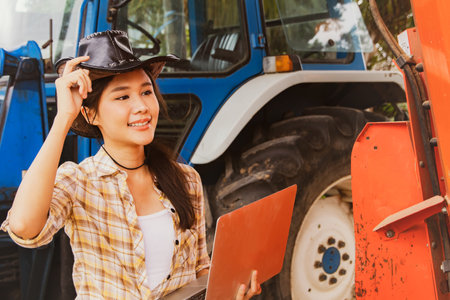 Asian woman farmer smile, agribusiness and livestock operator holding laptops to inspect machines and tractors for agricultural use, inspect maintenance services and use on agriculの写真素材