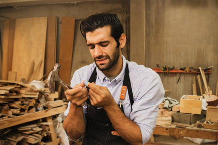 Handsome carpenter worker furniture factory Cried in pain from the accident that he was hammered in the finger by a hammer while working. First aid plasters are requiredの写真素材