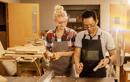 Caucasian female student thumbs up senior asian carpenter teacher teaches safe and easy to understand woodworking machine tools, showing careful demonstration of woodworking.の写真素材
