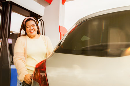 Asian woman driving car stops to refuel at a modern gas station on a highway, standing near self-service petrol dispenser : Fat woman excitedly refuels clean gasoline by herselfの写真素材