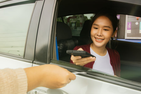 Asian woman drives a sedan, refuels at a gas station, pays for services by scanning barcodes with her smartphone, transfers money from credit cards instead of cash.の写真素材